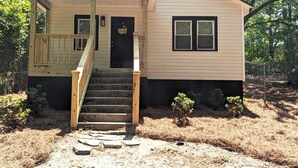 Une maison de plain-pied avec un porche à l’avant, un escalier menant à l’entrée et un petit jardin.