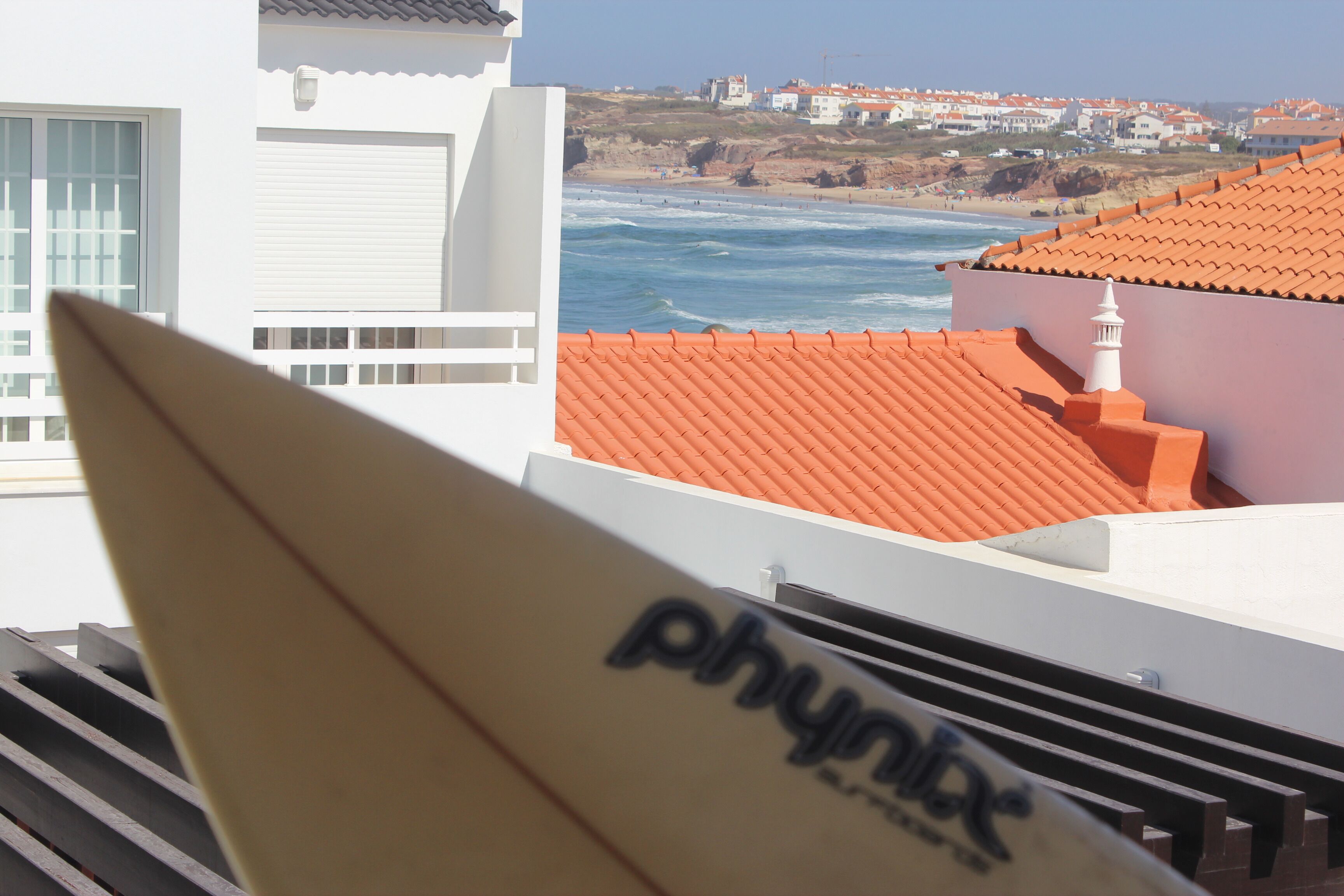 A coastal view with a white building and orange-tiled roofs.
