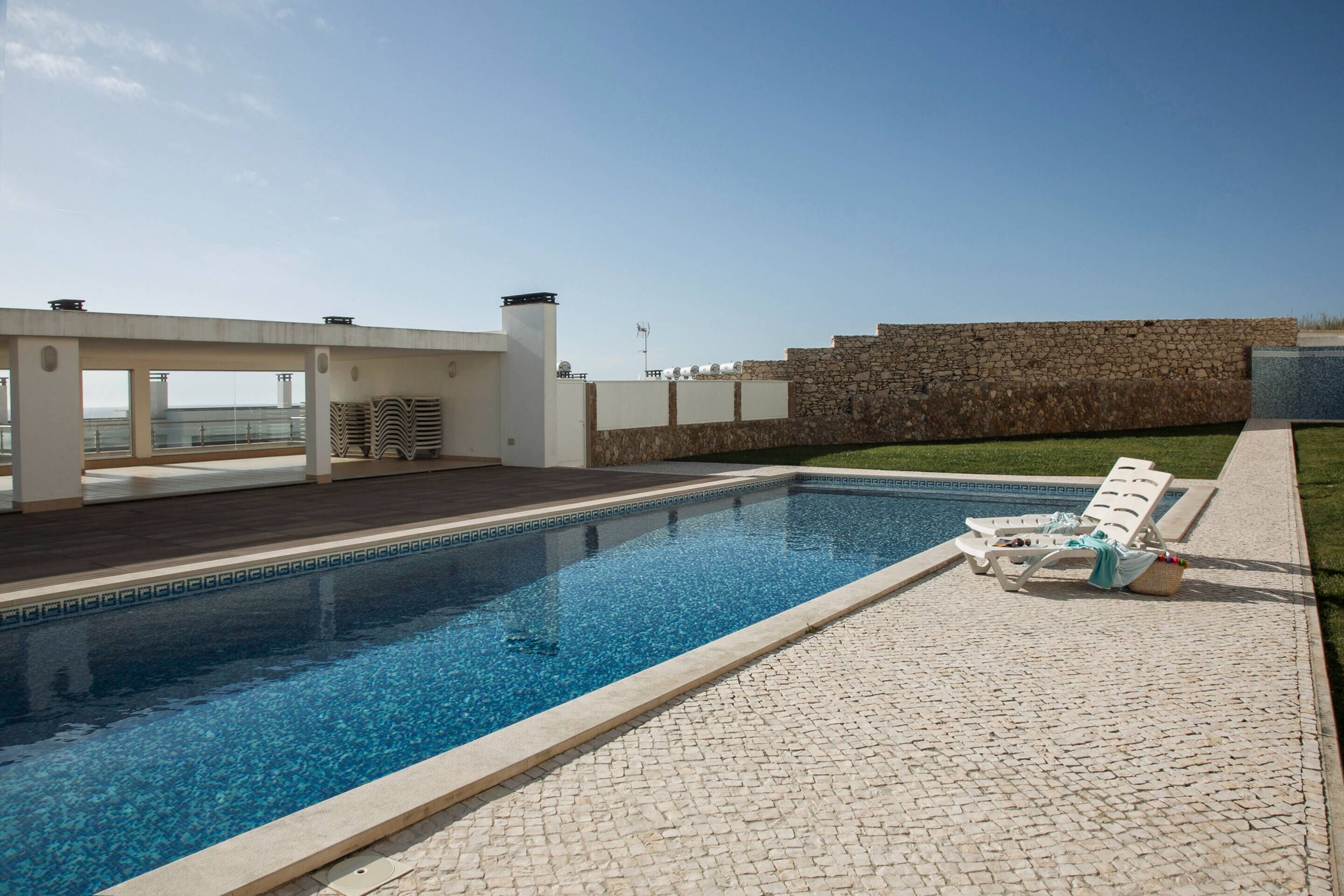 A rectangular swimming pool with a tiled edge, surrounded by a stone wall and a wooden deck.