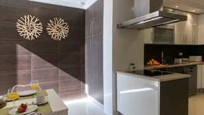 Een moderne keuken met een centraal eiland, donkere betegelde muren en een ontbijtsetting met sinaasappelsap en aardbeien.