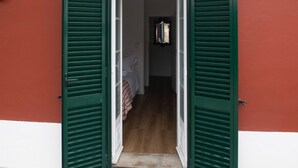 A hallway with green shutters leading to a bedroom with a bed and a window. - Casa Flamingo - Casa Principal, Foz do Arelho (Caldas da Rainha)