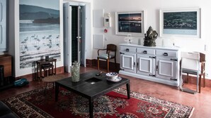 A spacious living room with a large window, a dining area, and a kitchen with white cabinets. - Casa Flamingo - Casa Principal, Foz do Arelho (Caldas da Rainha)