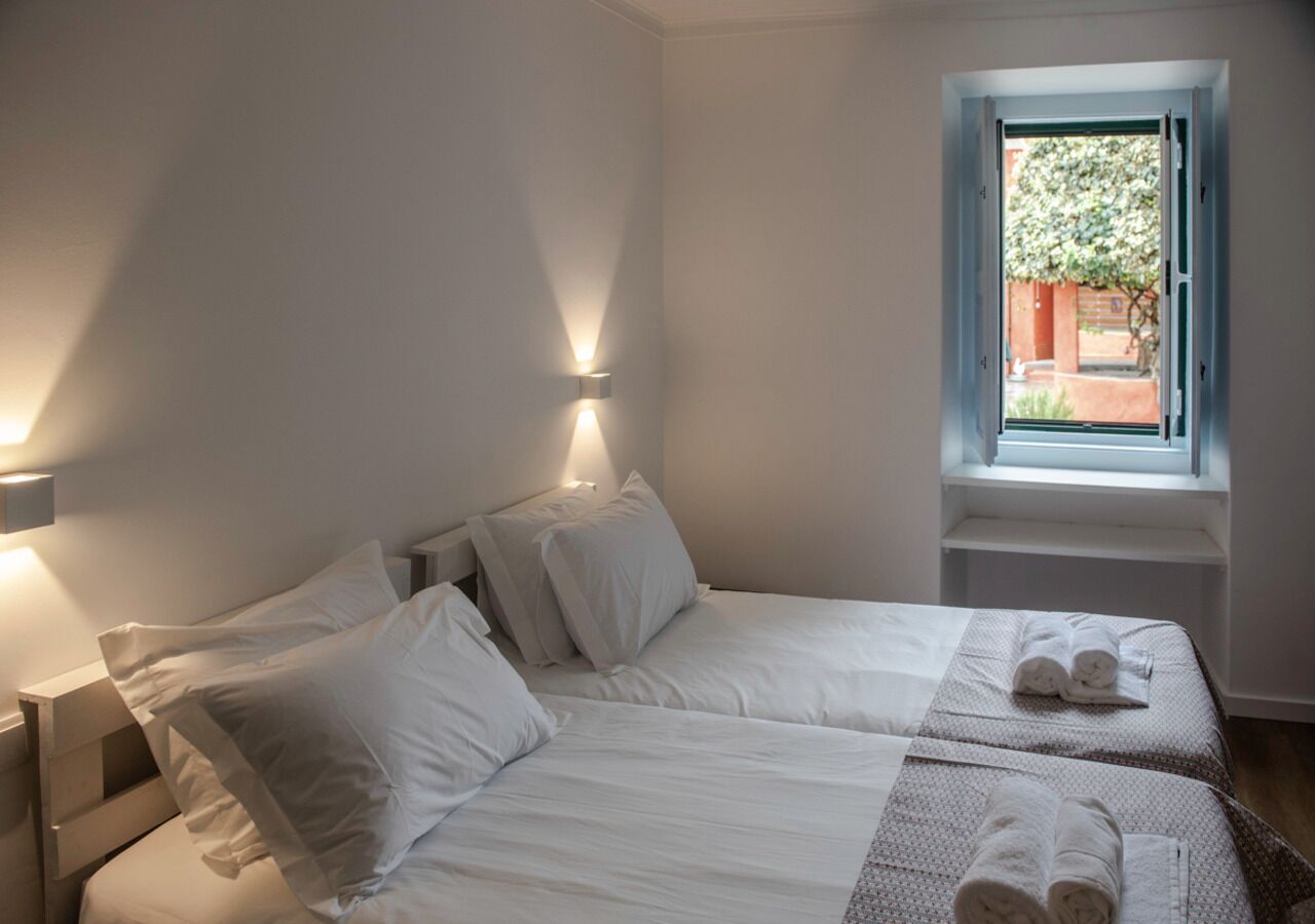 Een slaapkamer met twee bedden, een raam met uitzicht op groen en een handdoek op het bed.