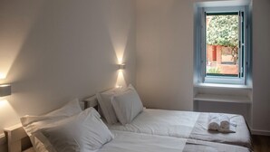 A bedroom with two beds, a window with a view of greenery, and a towel on the bed. - Casa Flamingo - Casa Principal, Foz do Arelho (Caldas da Rainha)
