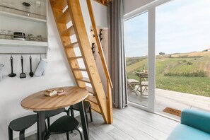 A modern interior with a wooden table, chairs, a ladder, and a view of a vineyard through large windows. - Quinta dos Castanheiros Studio (Óbidos)