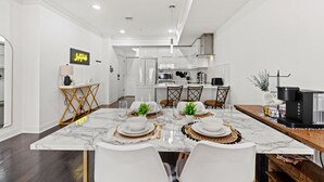 Una cocina moderna con armarios blancos, encimera de mármol y comedor con una mesa dispuesta para cuatro.