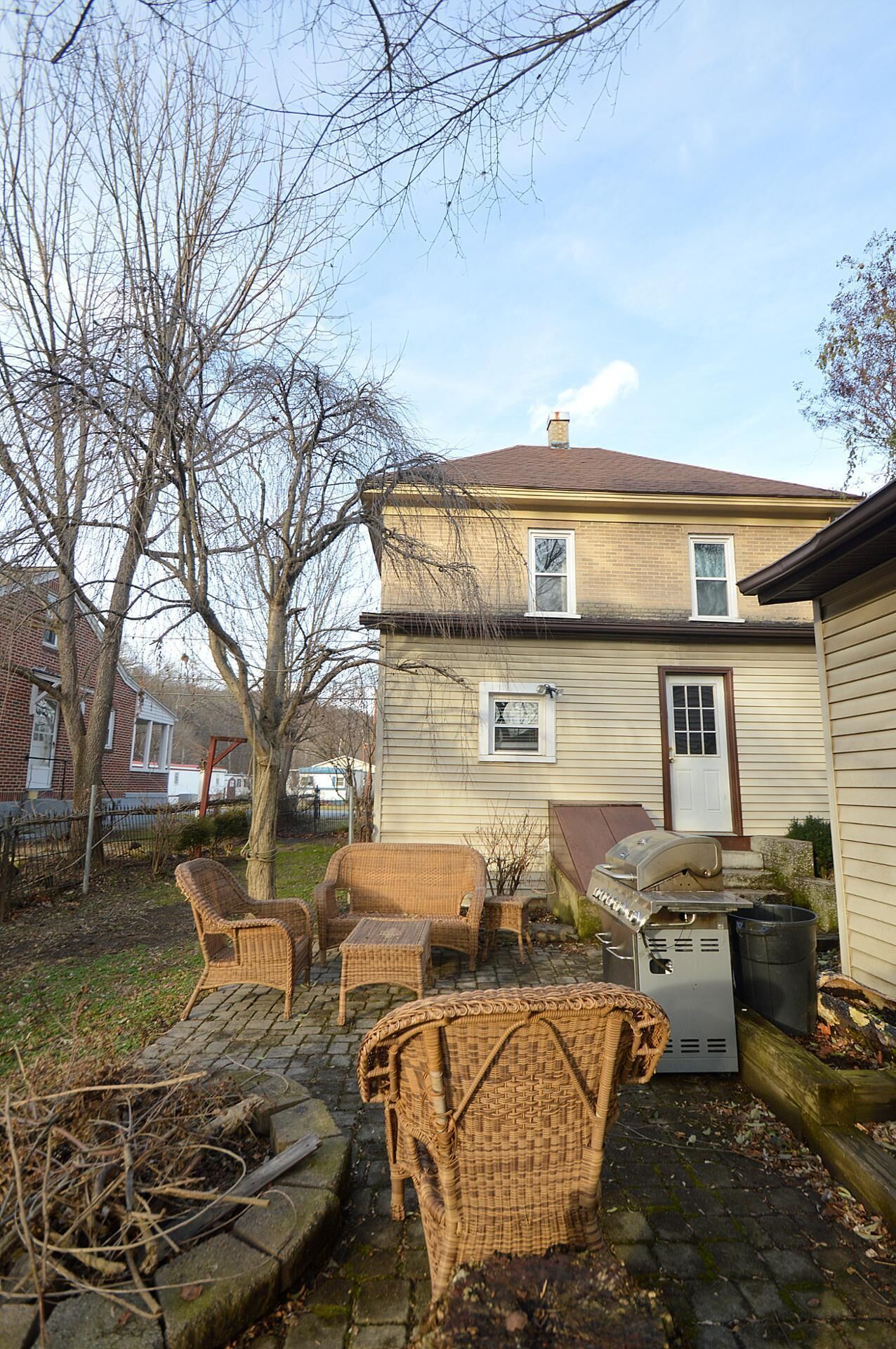 A house with a brick exterior, a chimney, and a front door. There is a patio with wicker furniture and a grill.