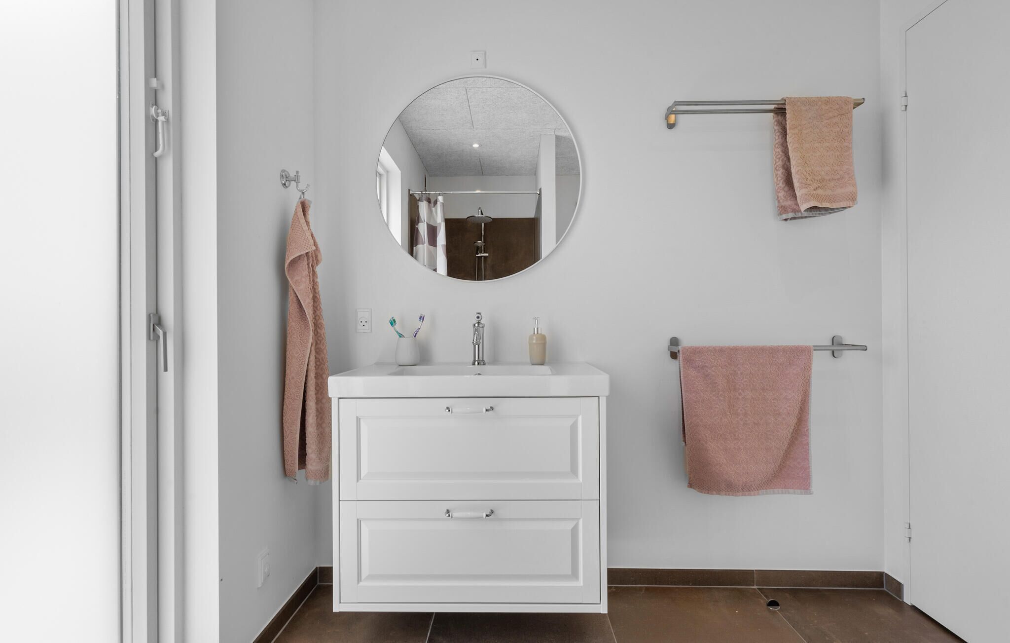 A bathroom with a white vanity, a round mirror, and two towels hanging on towel bars.