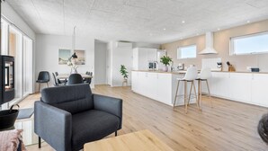 A modern kitchen with white cabinets, a wooden countertop, and a dining area with a grey sofa and a small table.