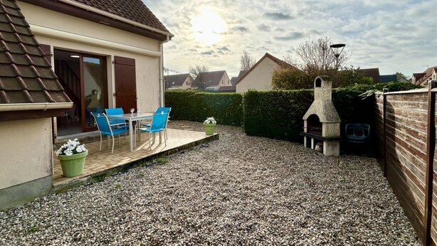 Un jardin à l’arrière d’une maison, comprenant une terrasse, un espace barbecue et un chemin de gravier.