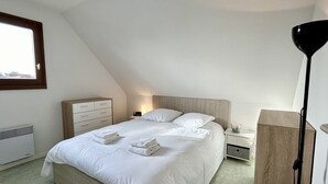Une chambre à coucher avec un lit, des tables de chevet, une lampe, un radiateur et une fenêtre.