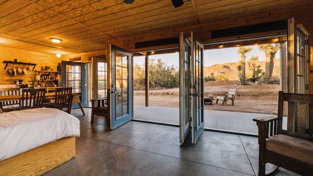 A spacious room with a large bed, a dining area with chairs, and open doors leading to an outdoor patio with desert views. - Joshua Tree Hidden Tower - View - Landmark - Across from National Park - Pets OK (Yucca Valley)