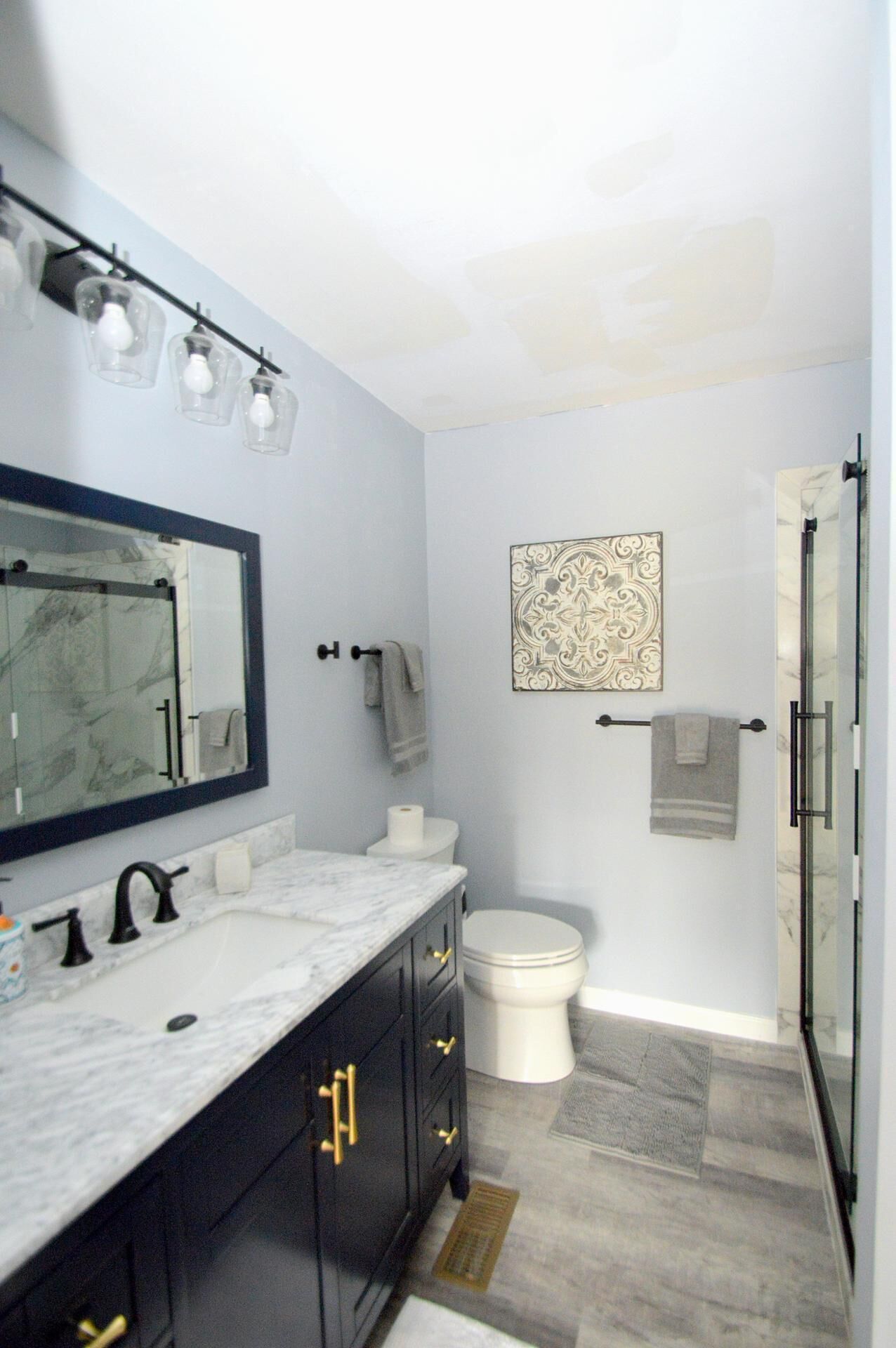 A modern bathroom with a marble sink, dark cabinetry, a large mirror, a toilet, and a shower area.