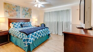 Ein Hotelzimmer mit Bett, Deckenventilator, Kunstwerk an der Wand, Schreibtisch und Fernseher.