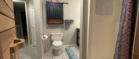 A bathroom with a toilet, a shower with a patterned curtain, and a small cabinet above the toilet.