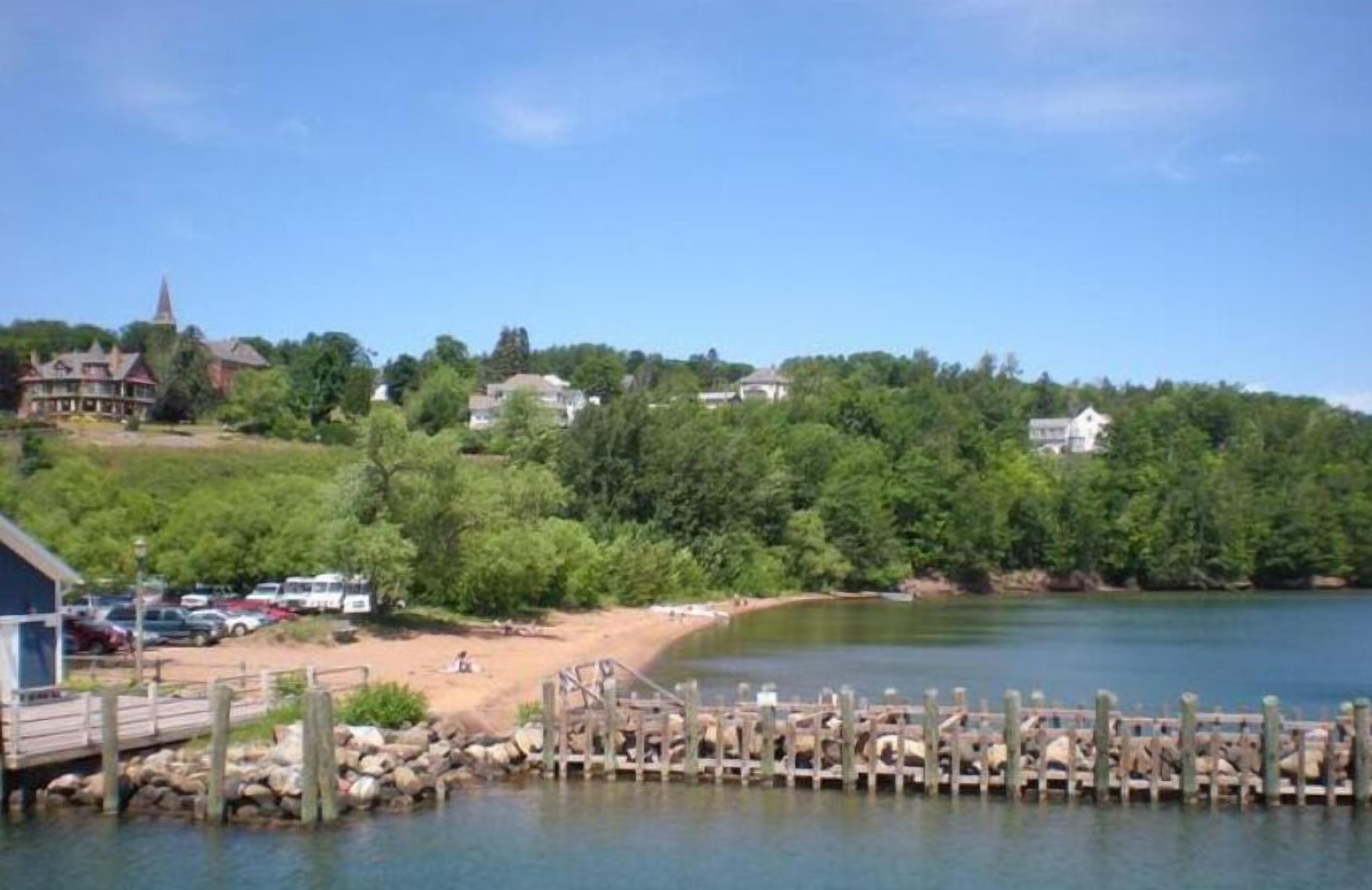 A lakeside property with a dock, a beach, and a church in the background.