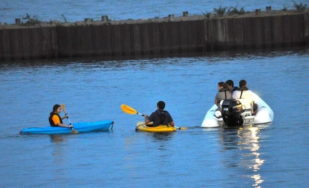 Three kayaks on calm water, a blue kayak on the left, a yellow kayak in the middle, and a white inflatable kayak on the right.