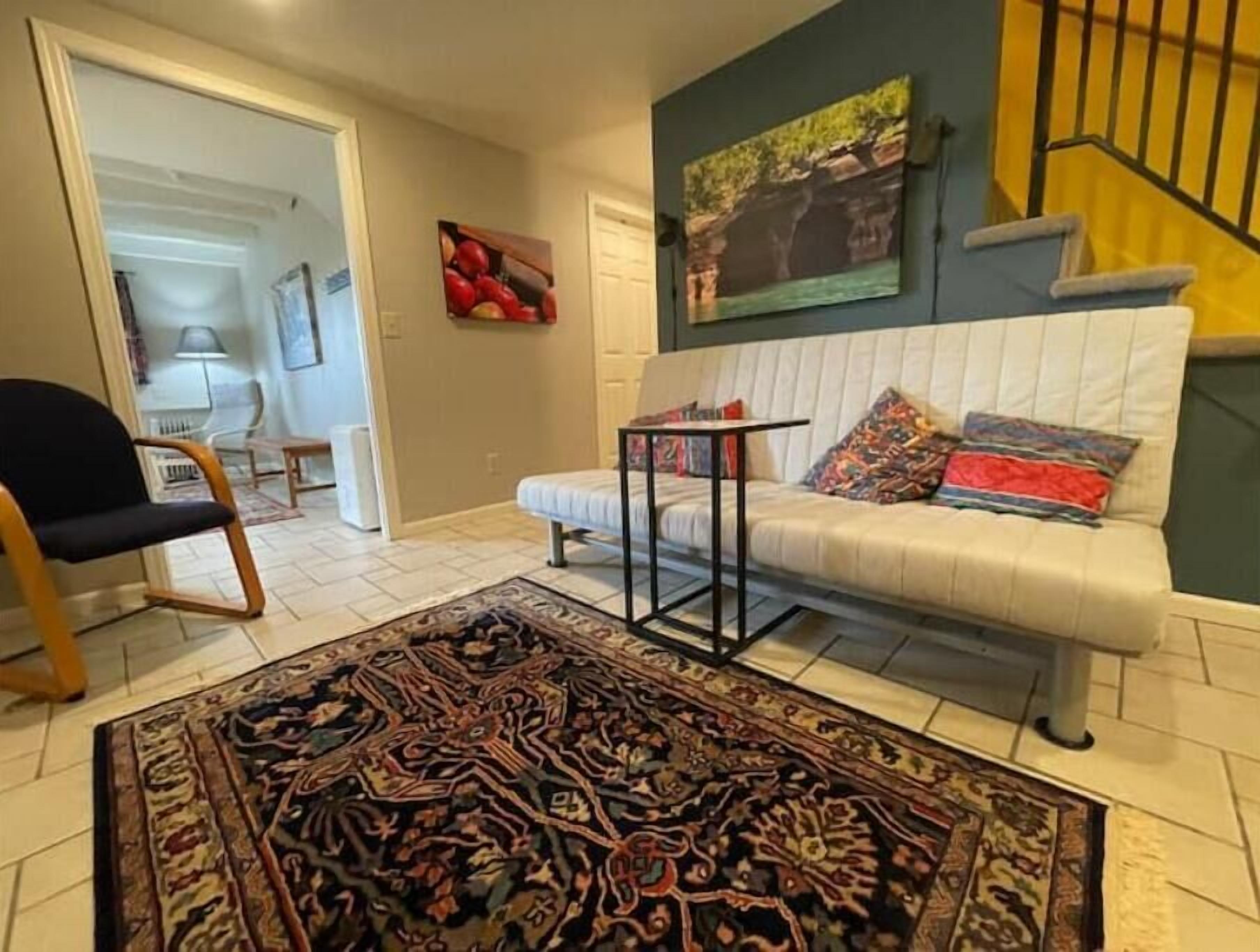 Een woonkamer met een witte bank, een tapijt met een patroon, een klein tafeltje en een schilderij aan de muur.