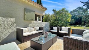 An outdoor patio with wicker furniture, a glass coffee table, and a white wall with shutters. - Lovely home in Nans-Les-Pins (Nans-Les-Pins)