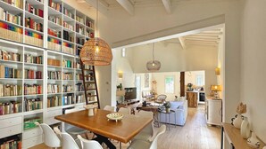 A spacious living area with a wooden dining table, white chairs, a bookshelf filled with books, and a kitchen in the background. - Lovely home in Nans-Les-Pins (Nans-Les-Pins)