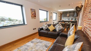 A spacious living room with a leather sofa, a patterned rug, and a city view through large windows. - Rooftops (St Ives)