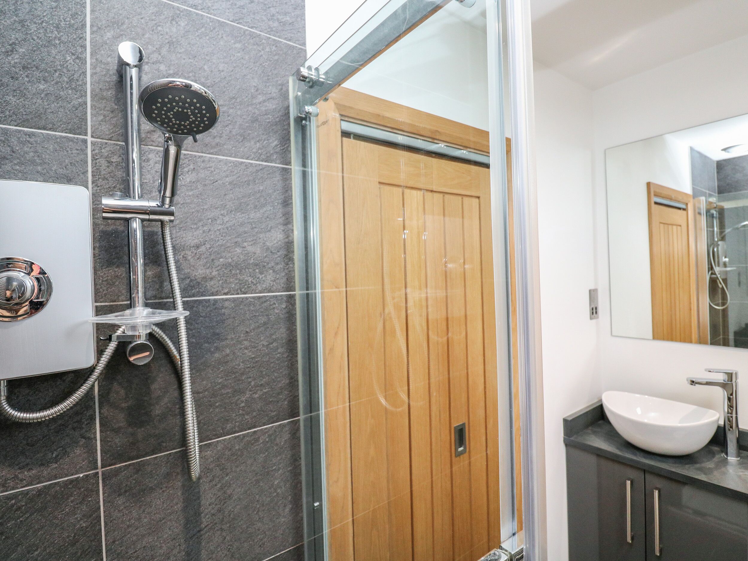 A modern bathroom with a glass-enclosed shower, a wooden door, and a large mirror.
