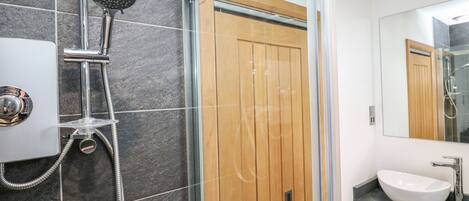 A modern bathroom with a glass-enclosed shower, a wooden door, and a large mirror.