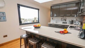 A modern kitchen with a large island, bar stools, a window with a city view, and stainless steel appliances. - Rooftops (St Ives)