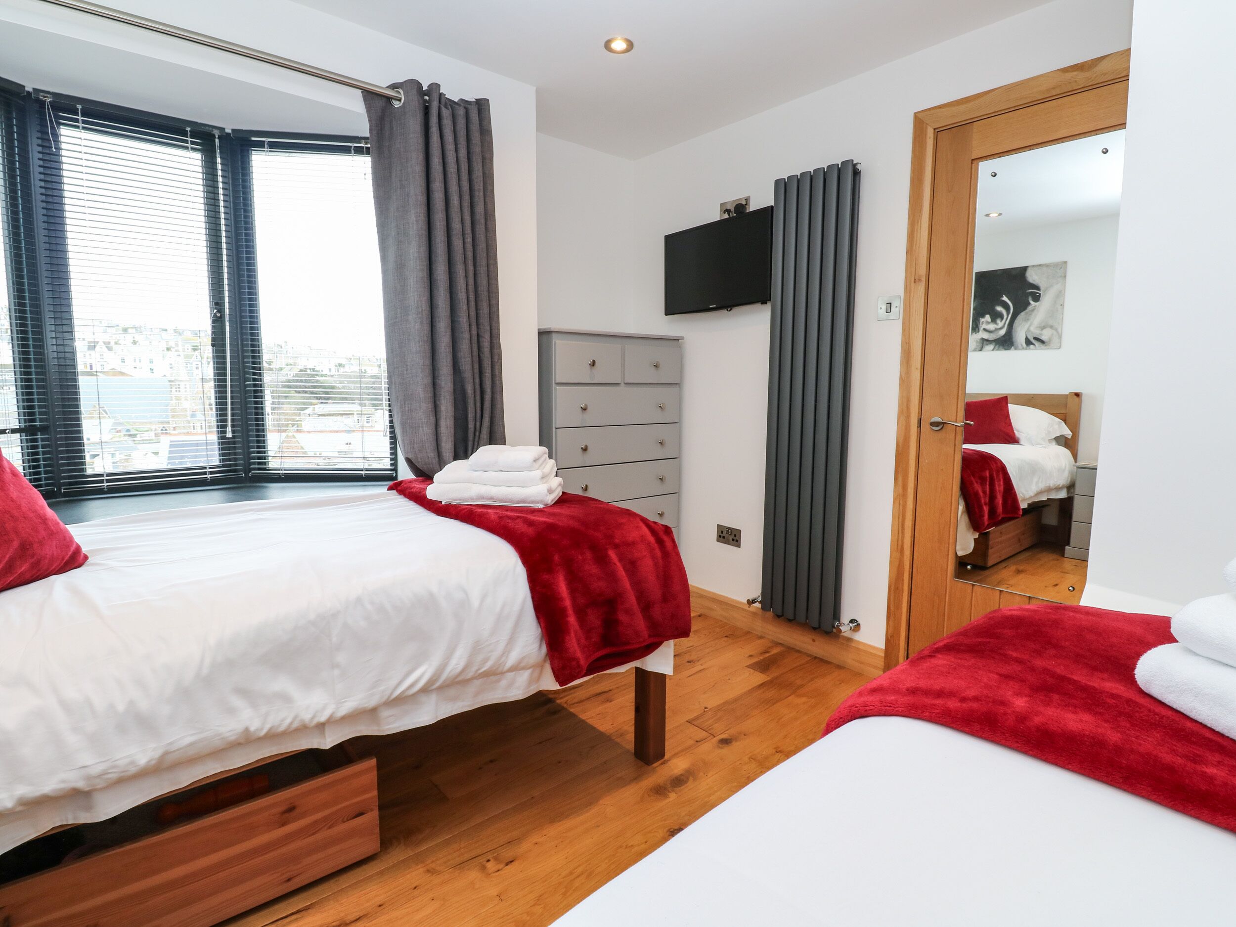 Une chambre moderne avec deux lits, une télévision, une commode et un miroir.