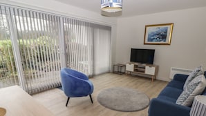 Een moderne woonkamer met een blauwe bank, een blauwe fauteuil, een tv-meubel en een schilderij aan de muur.