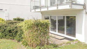 Een modern huis met twee verdiepingen, een balkon, een schuifdeur en een kleine tuin.