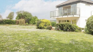 Una casa moderna de dos pisos con balcón, rodeada por un césped bien cuidado con flores blancas.