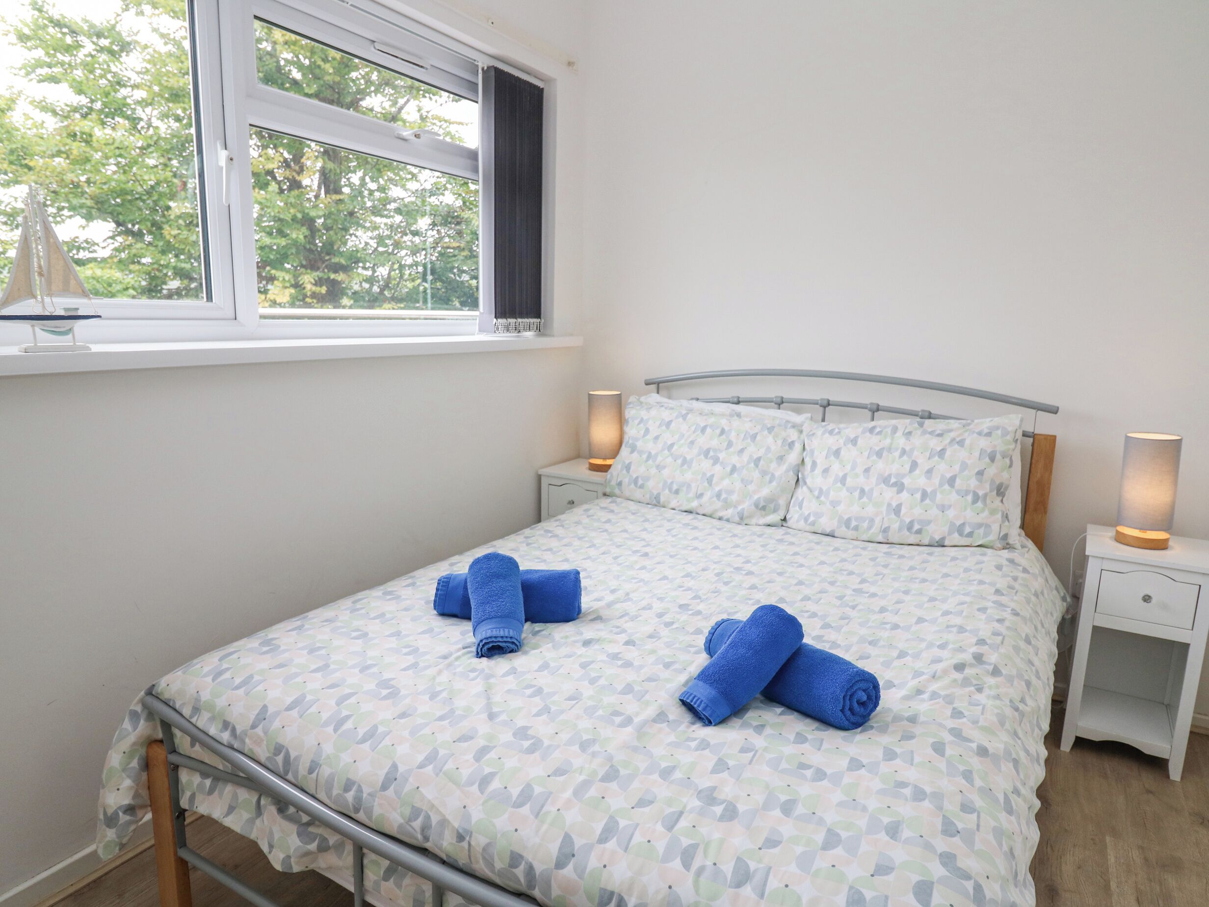 A neatly made bed with patterned bedding, two bedside lamps, and a window with a view of trees.