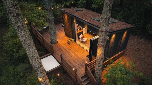 Una casa árbol con una terraza, un pequeño rincón de descanso y una escalera.