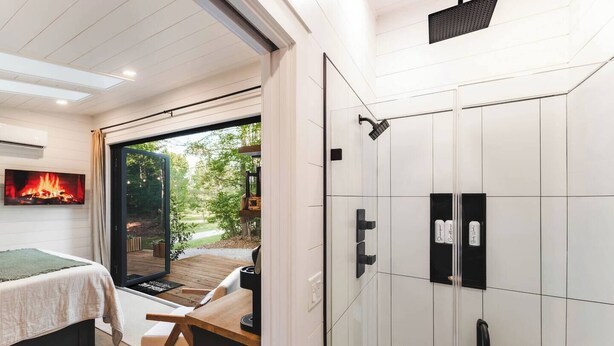 A modern bedroom with a large window, a bed, a wooden table, and a built-in wardrobe. - Luxury tiny house with hot tub and private deck! (Guntersville)