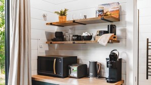 A modern kitchen with a microwave, toaster, coffee maker, and shelves with kitchenware. - Luxury tiny house with hot tub and private deck! (Guntersville)