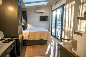 A compact bedroom with a bed, a desk, and a large window providing a view of the outdoors.