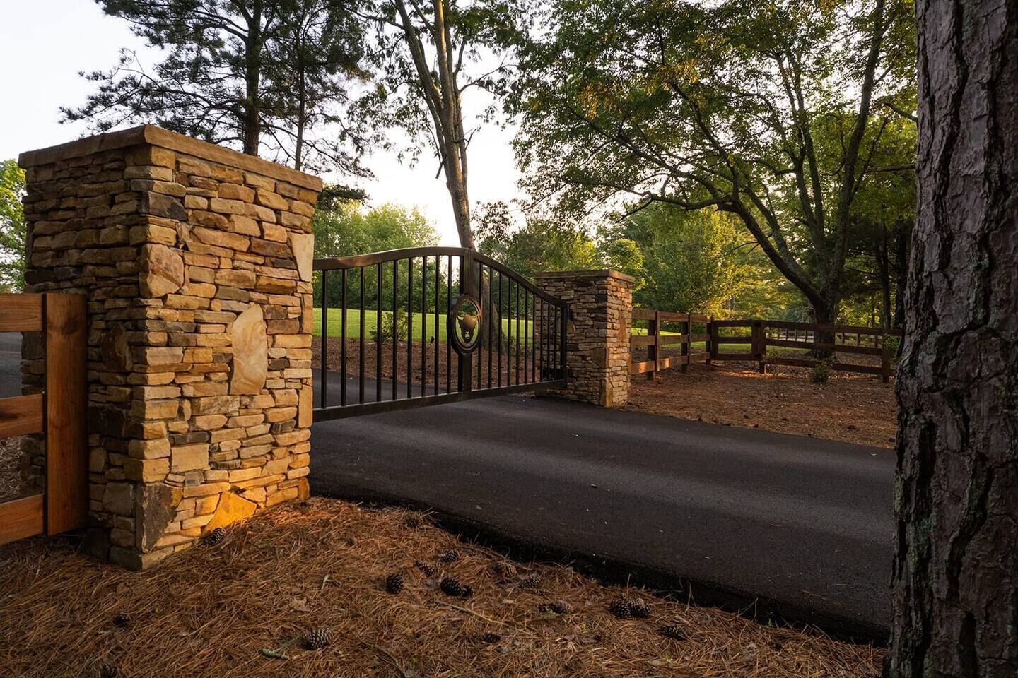 A stone gate with a metal fence, a paved path, and a wooden fence in a wooded area.