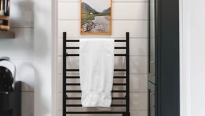 A bathroom with a towel rack, a framed picture on the wall, and a dark-colored cabinet. - Luxury tiny house with hot tub and private deck! (Guntersville)