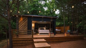 A cabin with a bed, a small table, and chairs on an outdoor deck. - Luxury tiny house with hot tub and private deck! (Guntersville)
