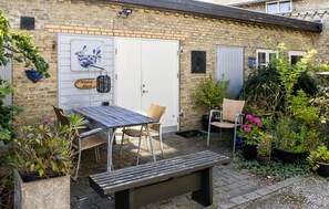 A brick house with a wooden table and chairs, a bench, and potted plants.