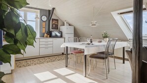 Une cuisine moderne avec un coin repas, comprenant une table blanche, des chaises en métal et une horloge au mur.
