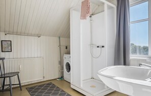 A modern bathroom with a walk-in shower, a built-in washing machine, and a large bathtub.