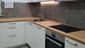 A modern kitchen with white cabinets, a wooden countertop, a stainless steel sink, a black induction cooktop, and a built-in oven. - WellandHome - 6 rooms (Aalen)