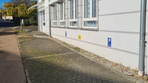 A building with multiple windows, a paved sidewalk, and a parking sign. - WellandHome - 6 rooms (Aalen)