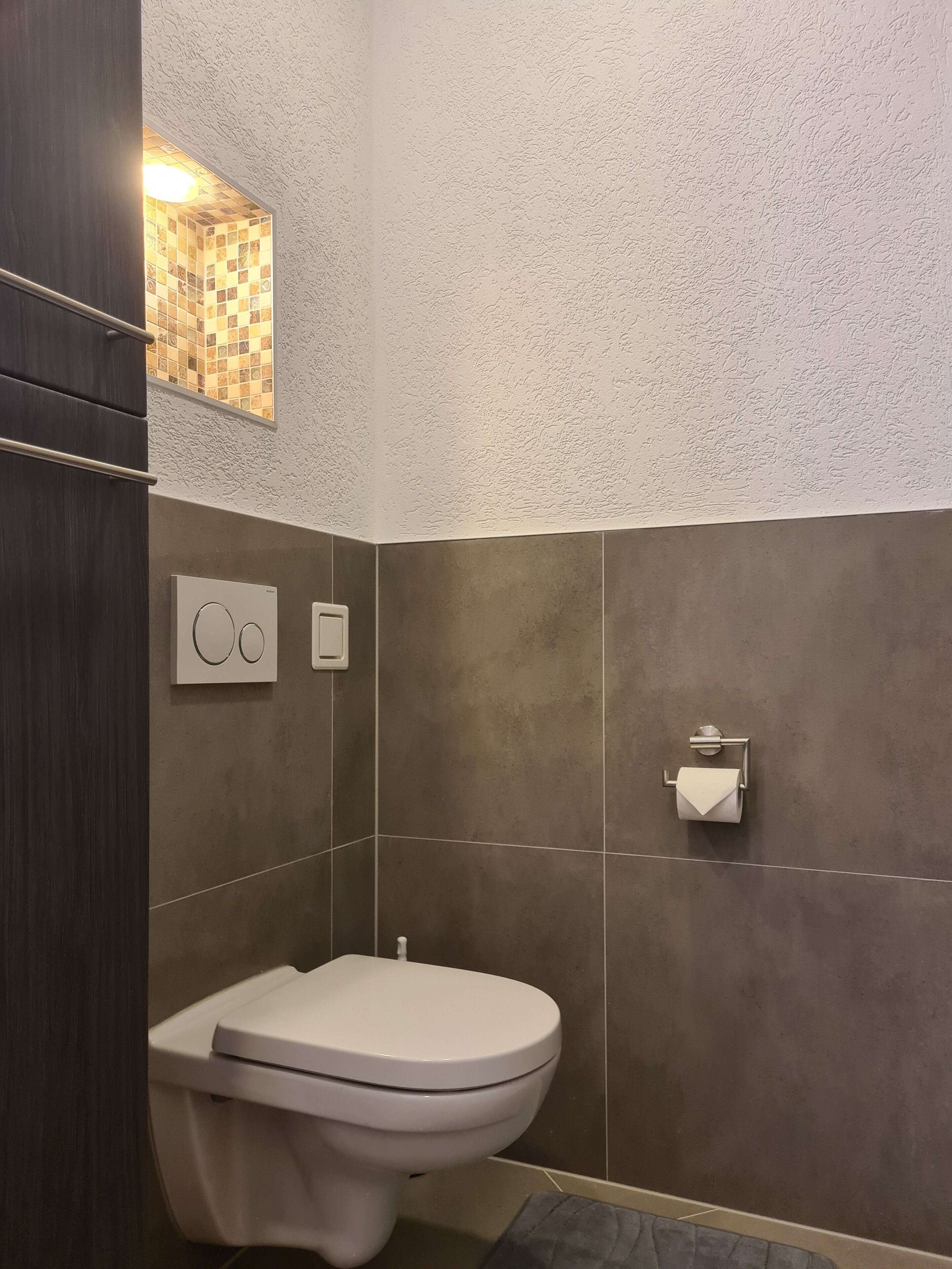 A modern bathroom with a toilet, a towel rack, and a wall-mounted light fixture.