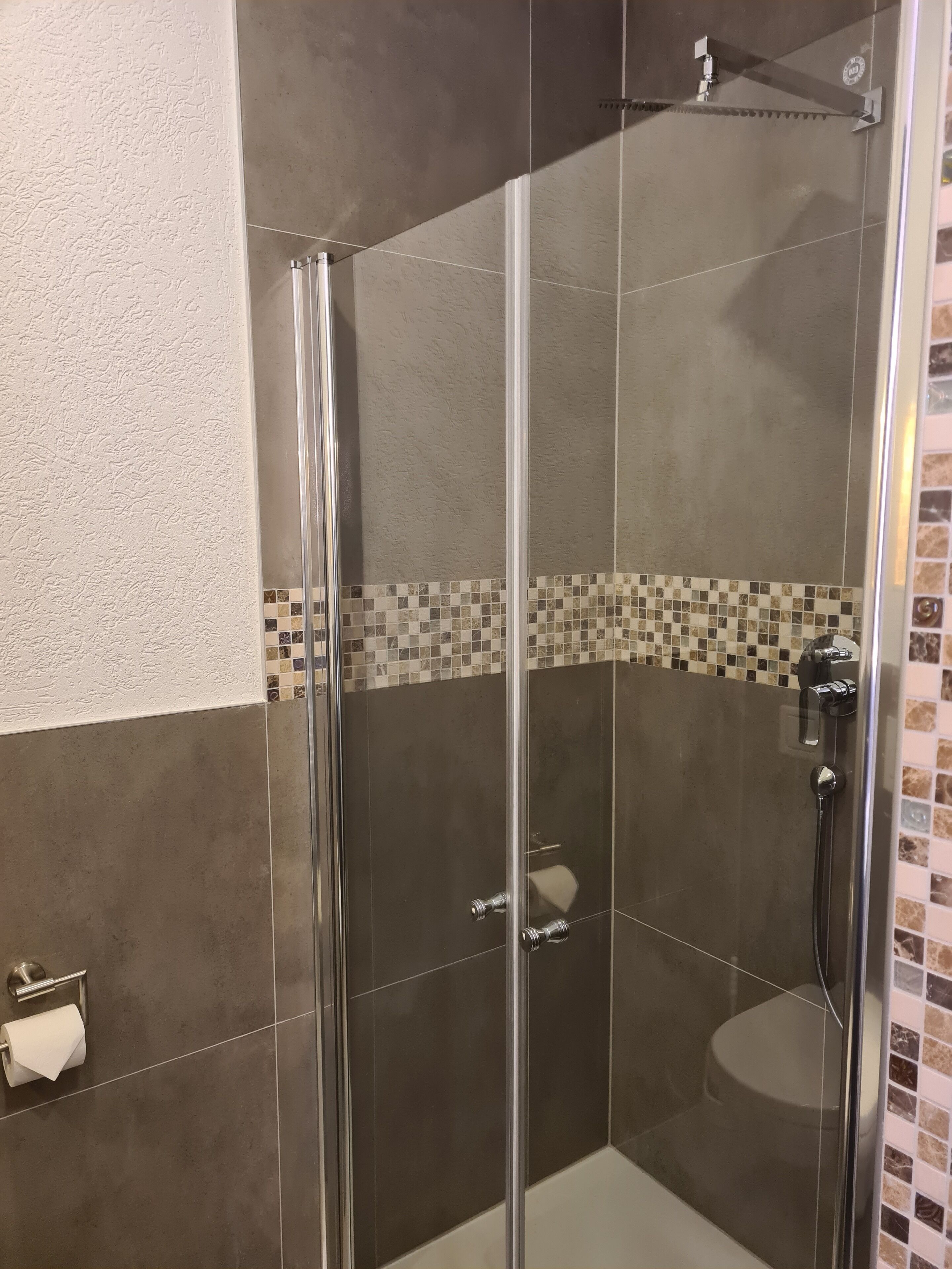 Una ducha con paredes de vidrio, suelo de baldosas y un lavamanos pequeño y redondo.