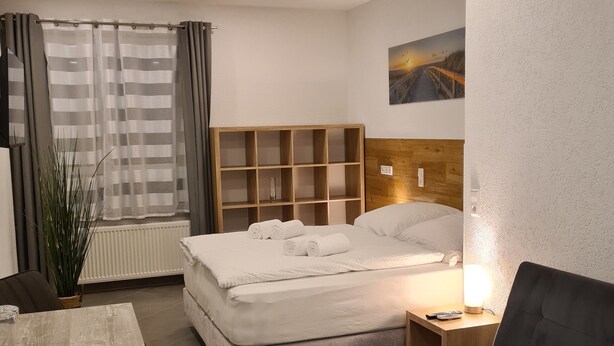 A modern hotel room with a bed, a sofa, a small table, and a bedside lamp. - WellandHome - 6 rooms (Aalen)