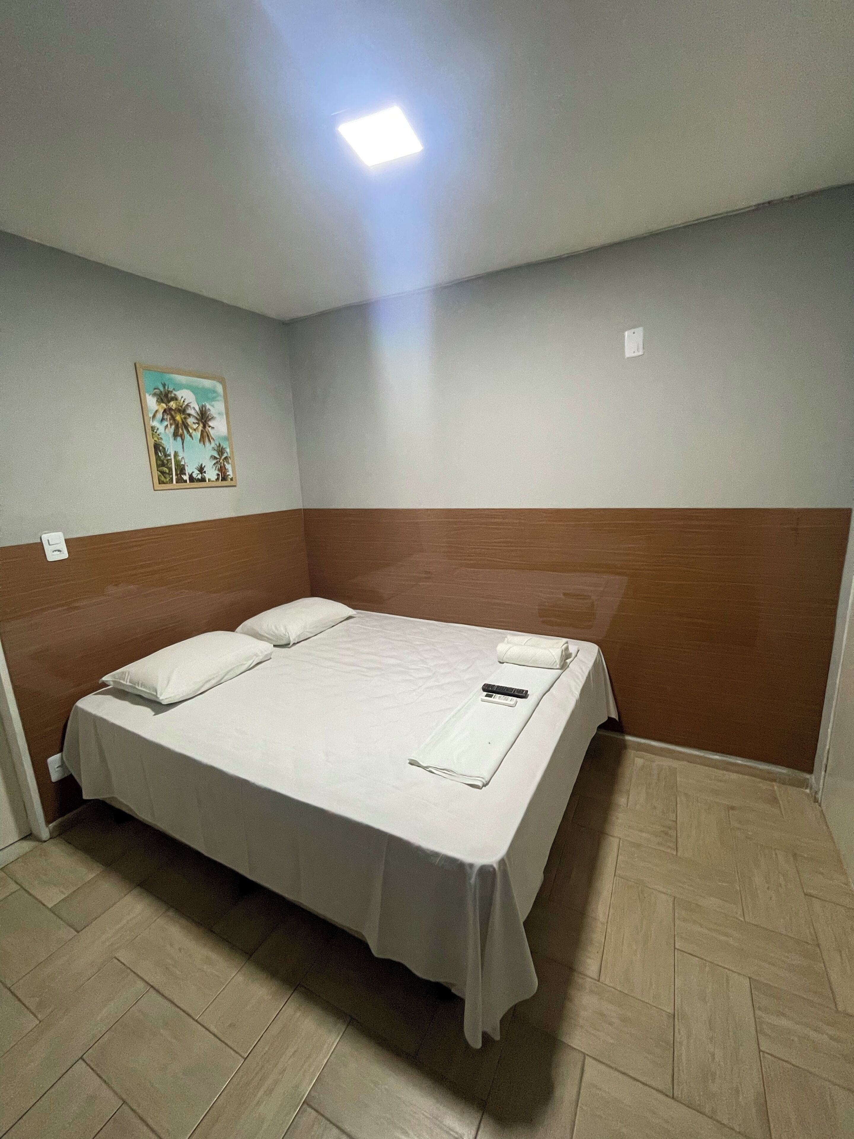 Une chambre d’hôtel avec un grand lit, une tête de lit en bois, un petit tableau accroché au mur et un sol carrelé.
