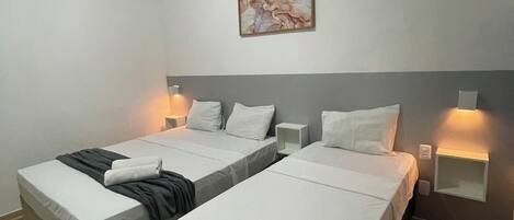 A hotel room with two single beds, a nightstand, a wall-mounted lamp, and a painting.